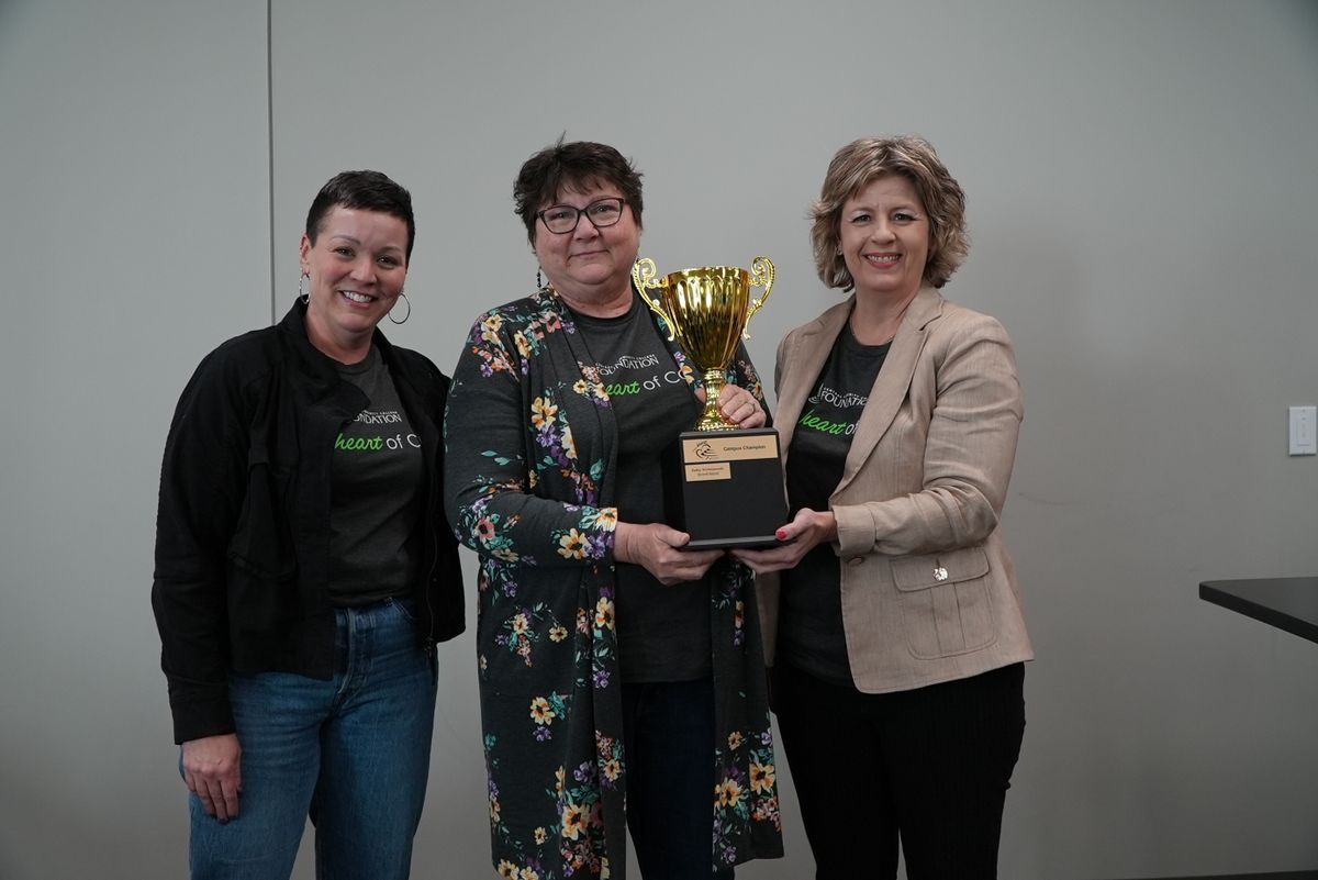 Three people standing, two are holding a trophy