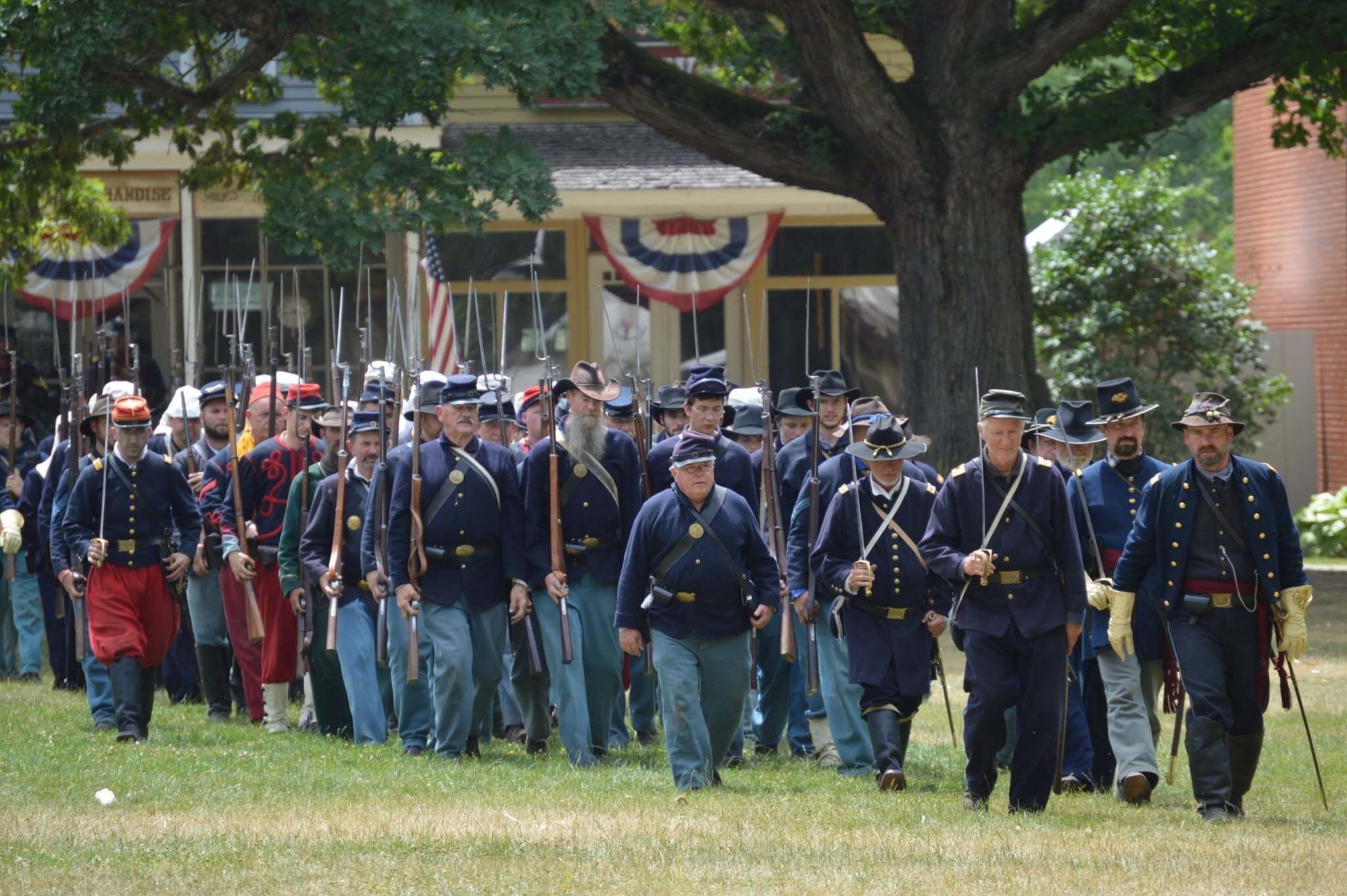 Civil War reenactors walking together in a line in blue coats and light blue pants carrying rifles.