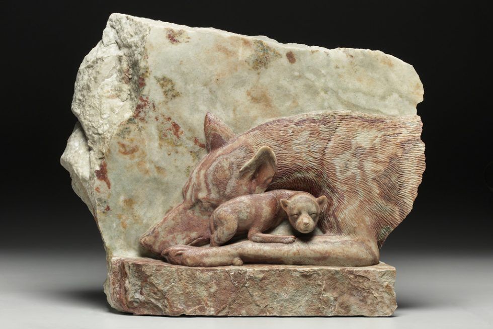 A red wolf mom and pup sculpture created from stone.