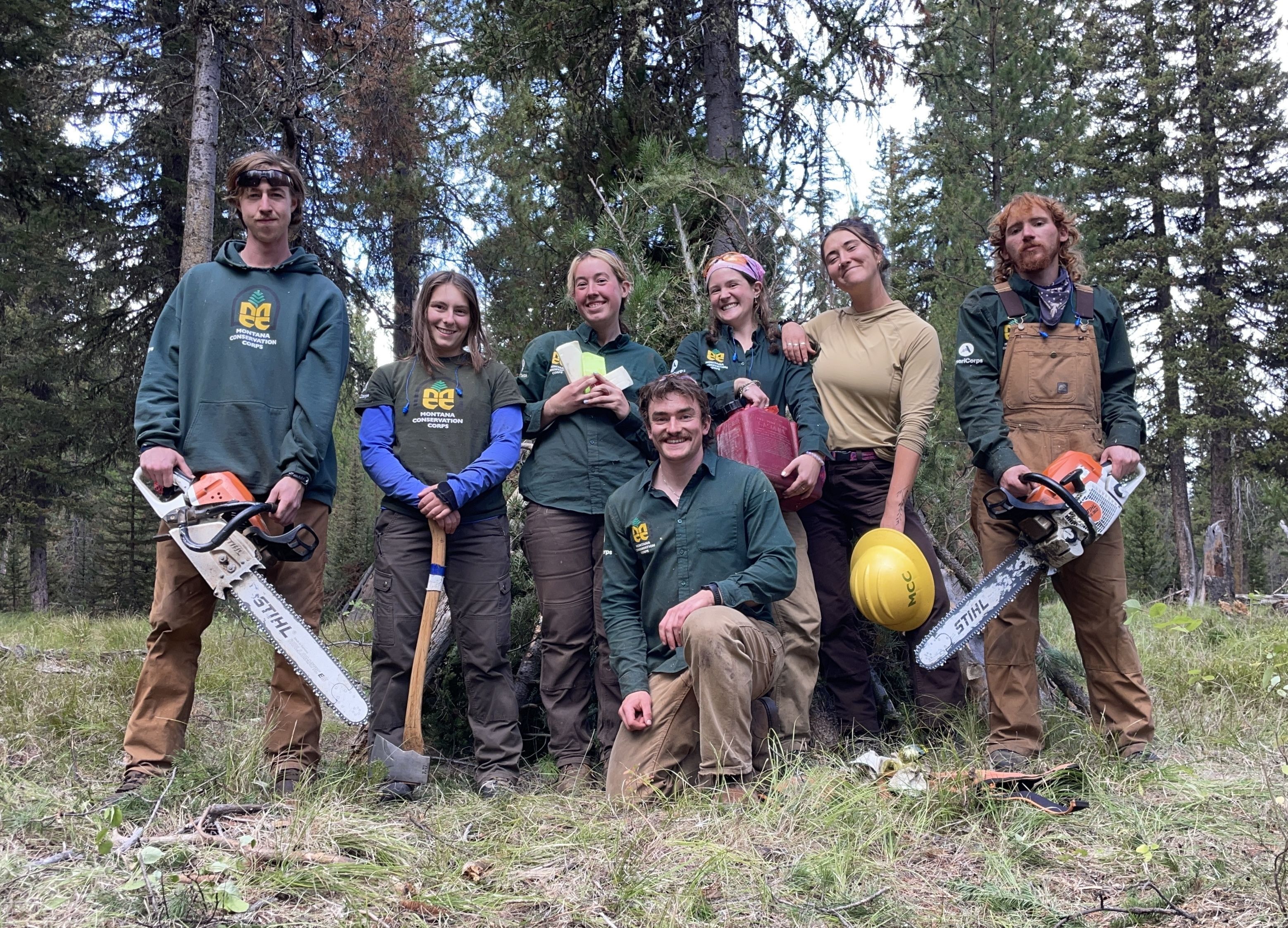Two crews stand holding chainsaws and smiling at the camera