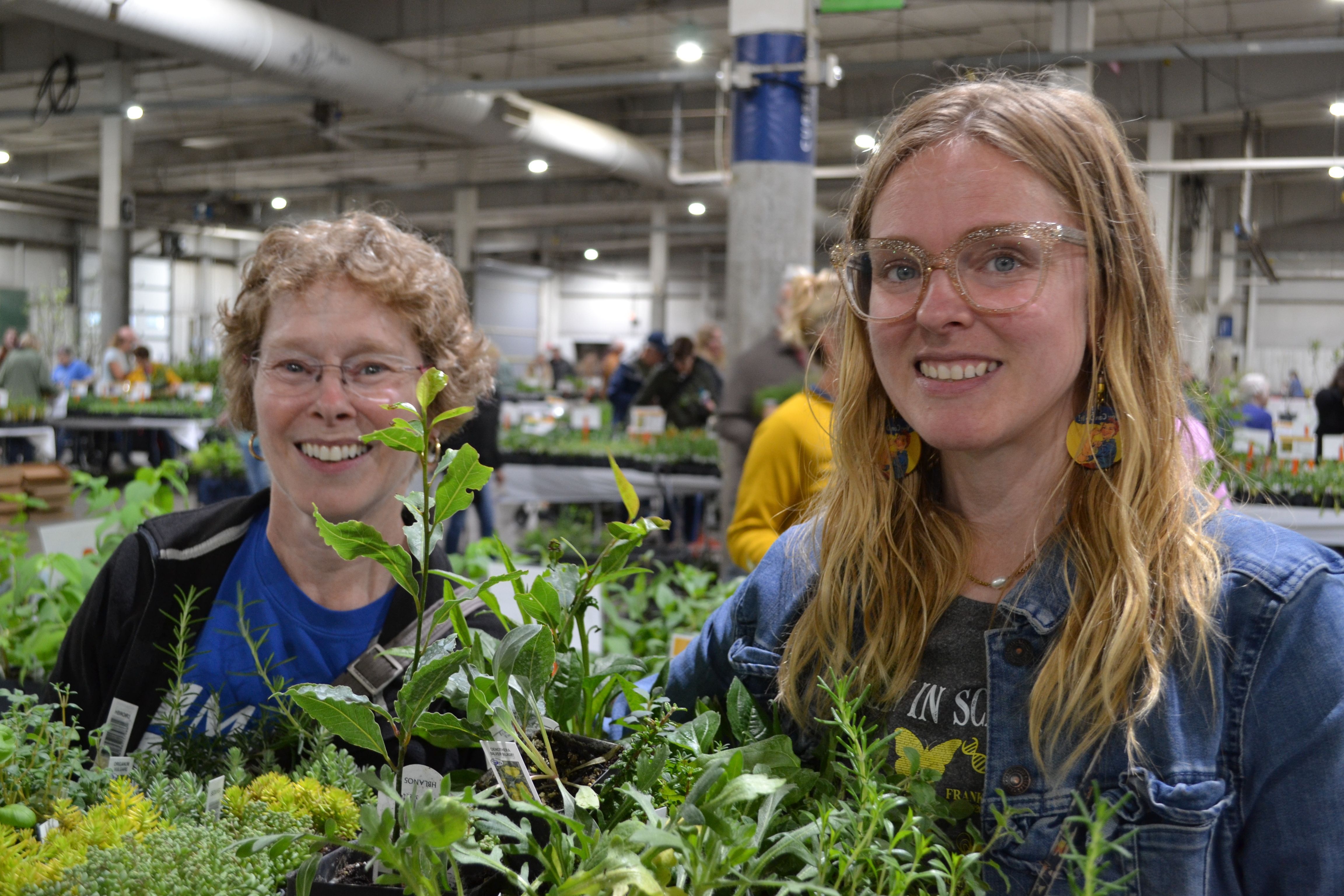 Two women hold a plant of flats at the Spring Affair Plant Sale. 