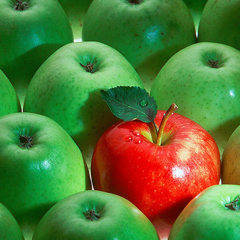 A red apple with a leaf among green apples.